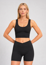 Femme portant un crop top de sport noir à brassière intégrée avec larges bretelles et un short cycliste noir assorti.