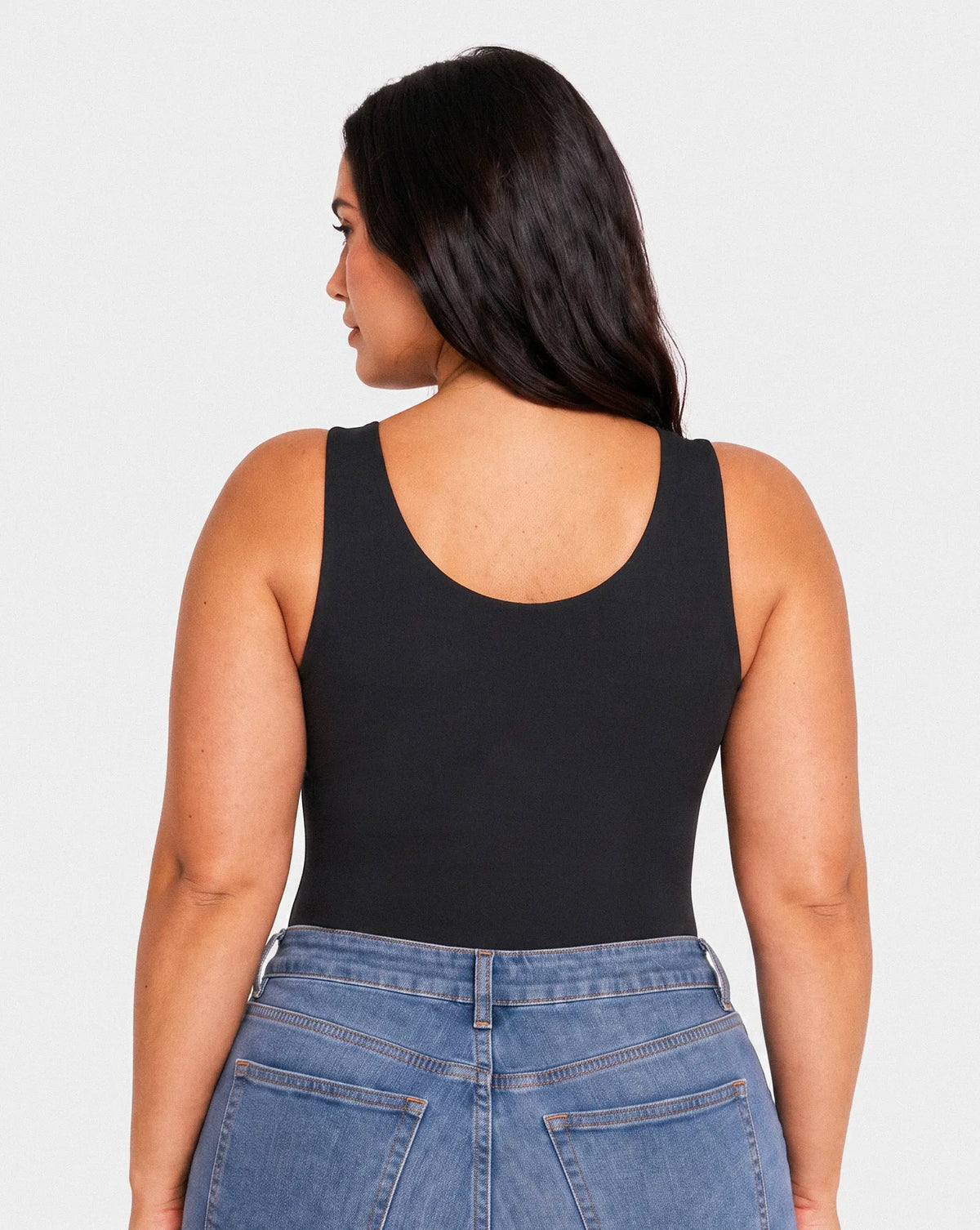 Femme vue de dos portant un top noir sans manches Onalie avec dos arrondi et un jean bleu taille haute.