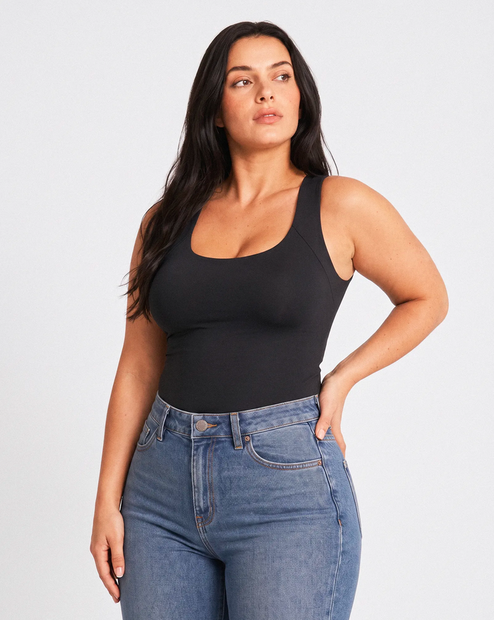 Femme portant un top noir sans manches Onalie avec jean bleu taille haute, vue de trois quarts.