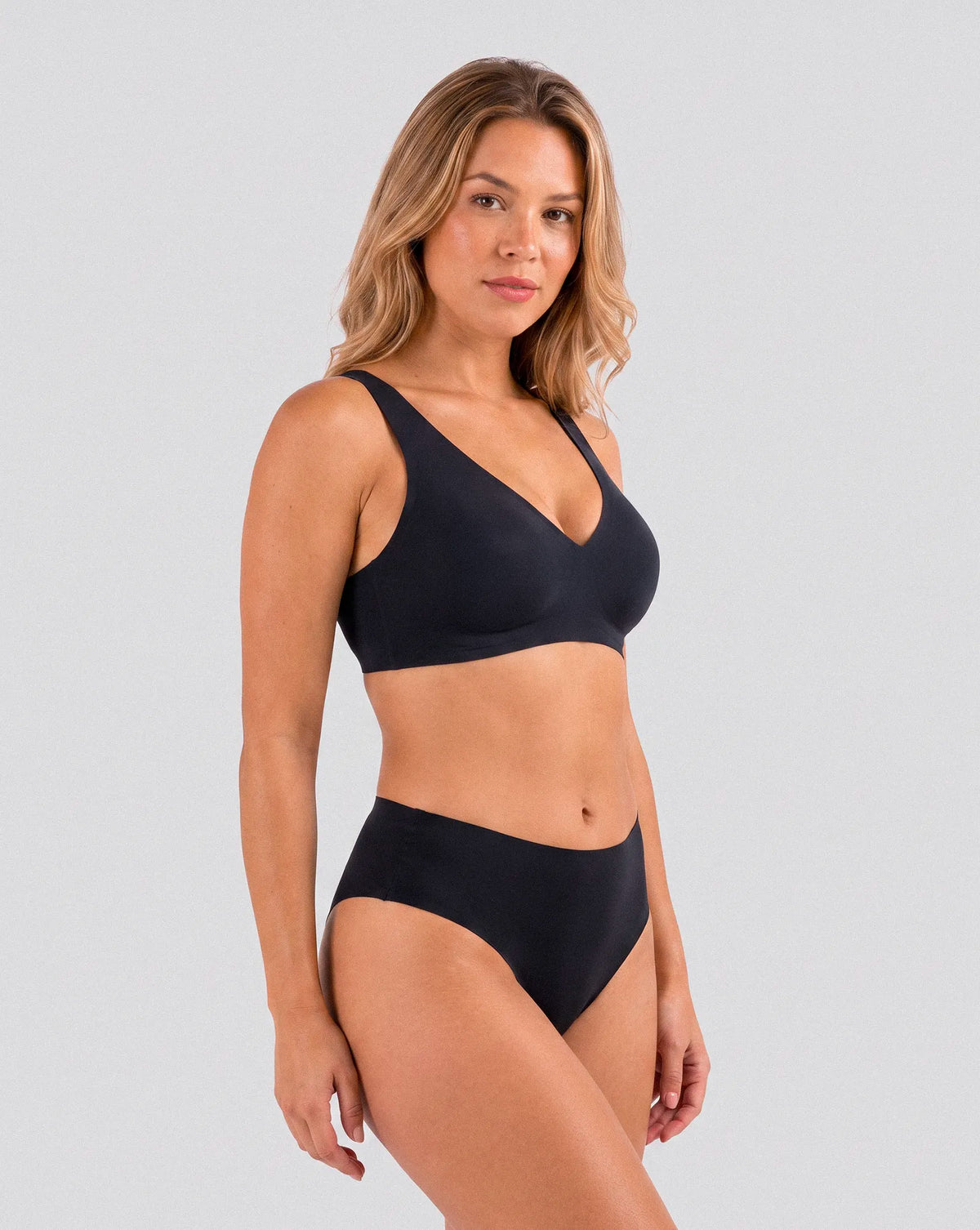 Femme portant le soutien-gorge noir sans armatures Onalie avec bas assorti, vue trois-quarts sur fond studio gris clair.