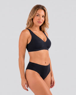 Femme portant le soutien-gorge noir sans armatures Onalie avec bas assorti, vue trois-quarts sur fond studio gris clair.