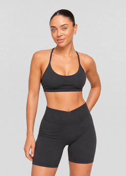 Femme portant un top court de sport noir à brassière intégrée et fines bretelles avec un short cycliste assorti.