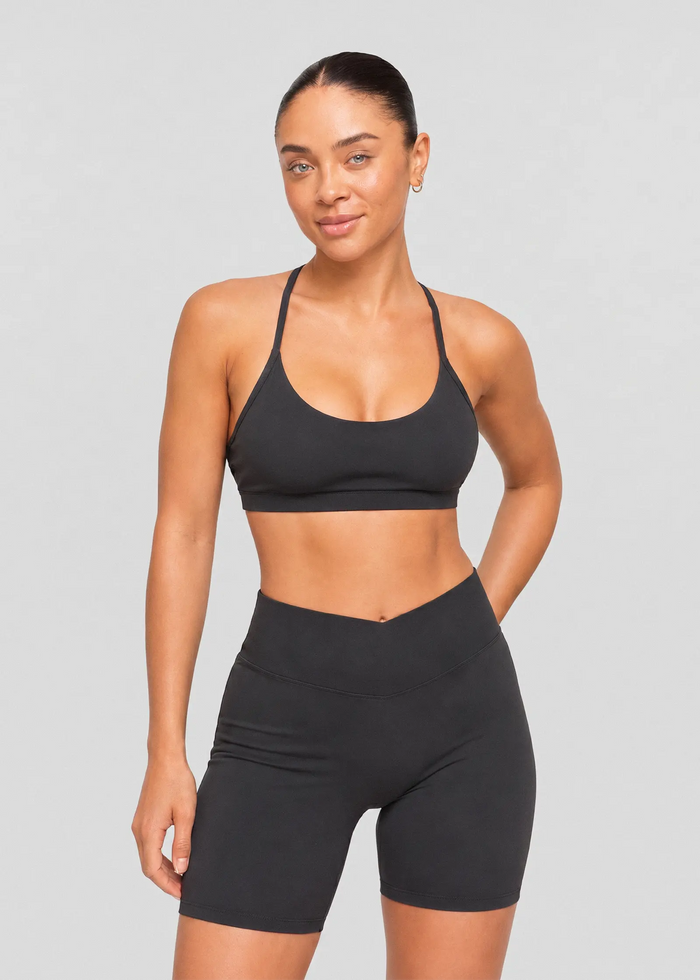 Femme portant un top court de sport noir à brassière intégrée et fines bretelles avec un short cycliste assorti.