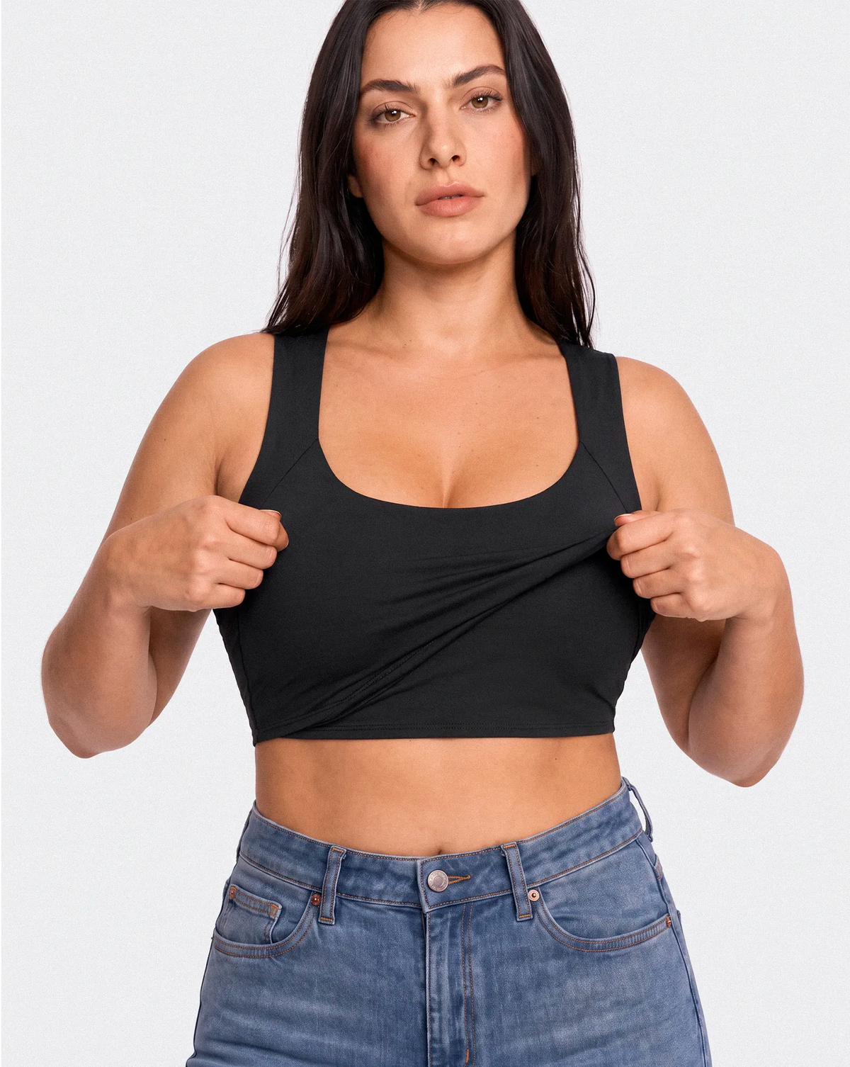 Femme portant un top noir avec brassière intégrée et montrant la couche extérieure extensible du vêtement.