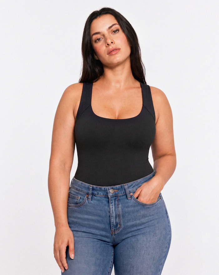 Femme portant un top noir à brassière intégrée avec un jean bleu, photographiée de face sur fond clair.
