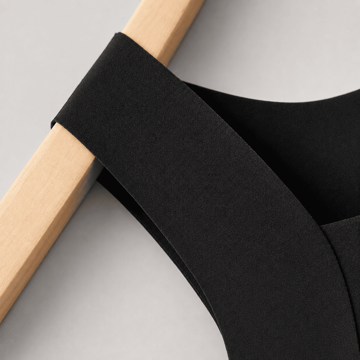 Bretelle large sans coutures du top noir sculptant Onalie posée sur un cintre en bois.